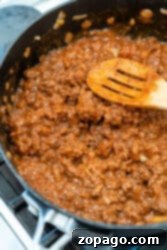 Cooking ground beef with onions and tomato sauce in a pan, stirred gently with a wooden spoon, is perfect for pairing with classic Sloppy Joe sides.