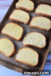 A baking sheet with eight slices of Texas toast, each coated in butter, set on a light wooden surface. The bread slices are evenly spaced and lightly toasted around the edges, perfect for making sloppy joes.