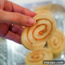 Close-up of a hand holding a cinnamon roll swirl with more frozen cinnamon rolls in the background.