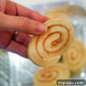 Close-up of a hand holding a cinnamon roll swirl with more frozen cinnamon rolls in the background, illustrating the recipe.