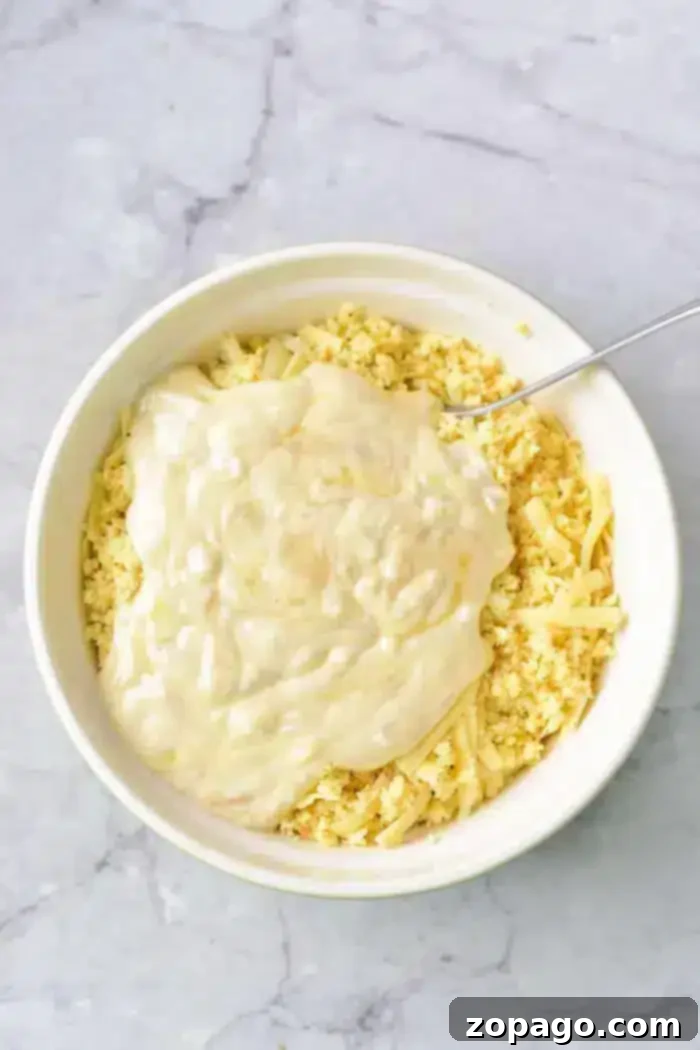 Easy 5 Ingredient Hash Brown Casserole 4 A white bowl contains shredded cheese and breadcrumbs, topped with a thick, creamy sauce, all the makings of a rich and flavorful 5 Ingredient Hash Brown Casserole.