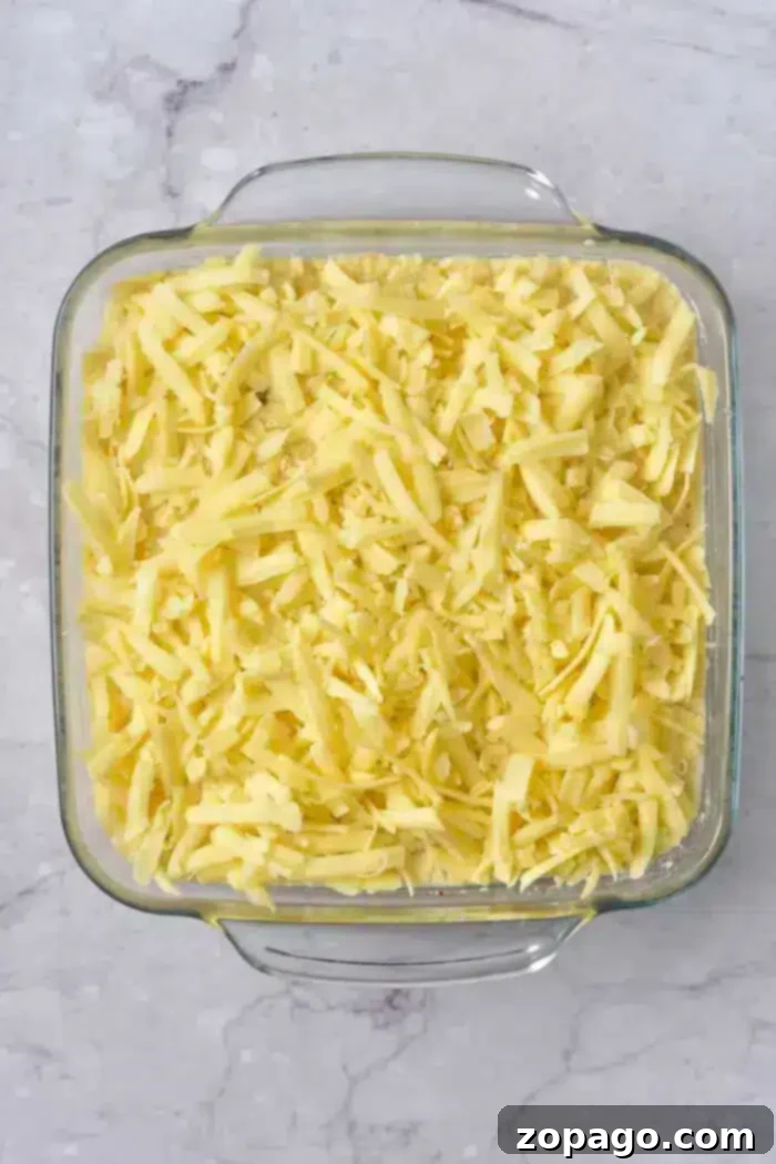 Easy 5 Ingredient Hash Brown Casserole 5 A clear glass baking dish filled with a generous layer of shredded cheese, perfectly prepared for a cheesy 5 Ingredient Hash Brown Casserole, sits on a cool marble countertop.