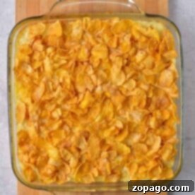 Easy 5 Ingredient Hash Brown Casserole 7 A glass baking dish filled with a 5 Ingredient Hash Brown Casserole, topped with crispy cornflakes, sits invitingly on a wooden board.