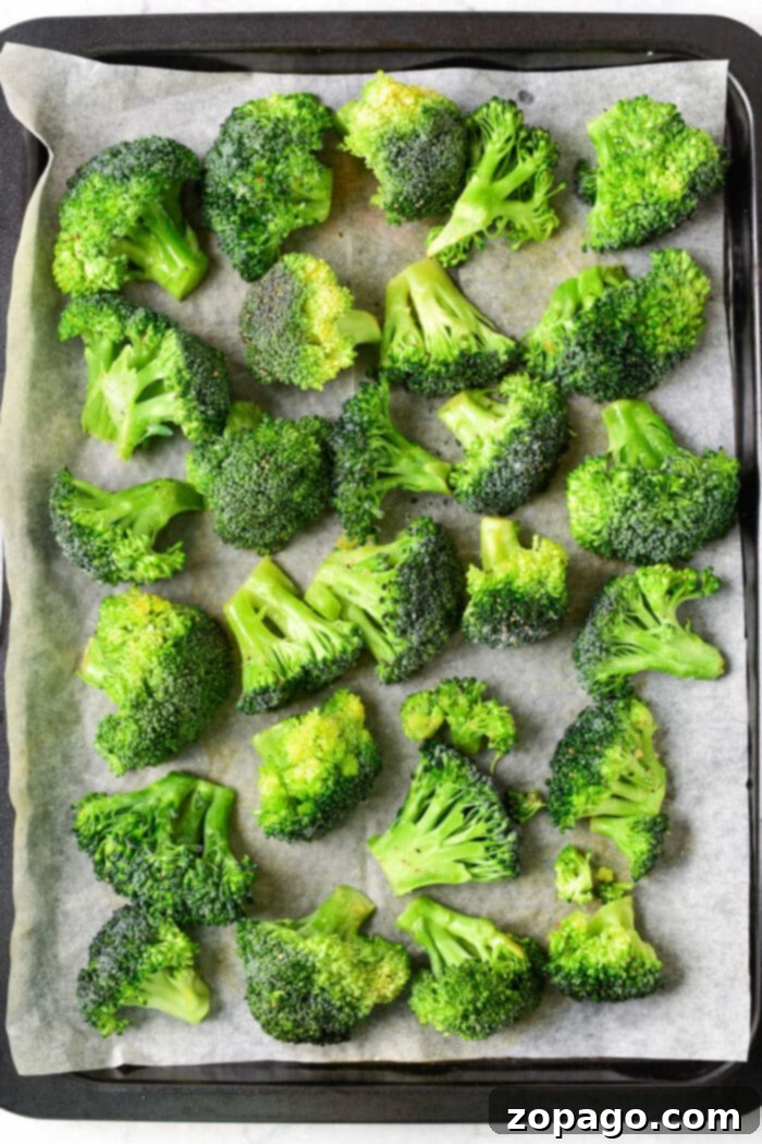 Perfectly Baked Frozen Broccoli 4 Uncooked frozen broccoli florets tossed with olive oil and seasoning on a parchment-lined baking sheet, ready for the oven.