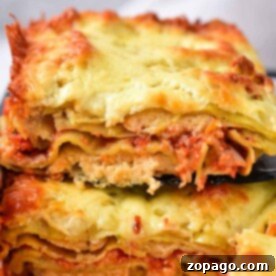 Two slices of cheesy, baked lasagna stacked on a black spatula, showcasing layers of pasta, sauce, and cheese, capture the essence of comfort food reminiscent of homemade baked ravioli delights.