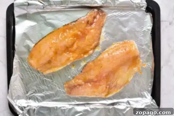 Two raw fish fillets, perfectly sauced, are placed on a foil-lined baking tray, ready to transform into a delightful meal as they bake from frozen.
