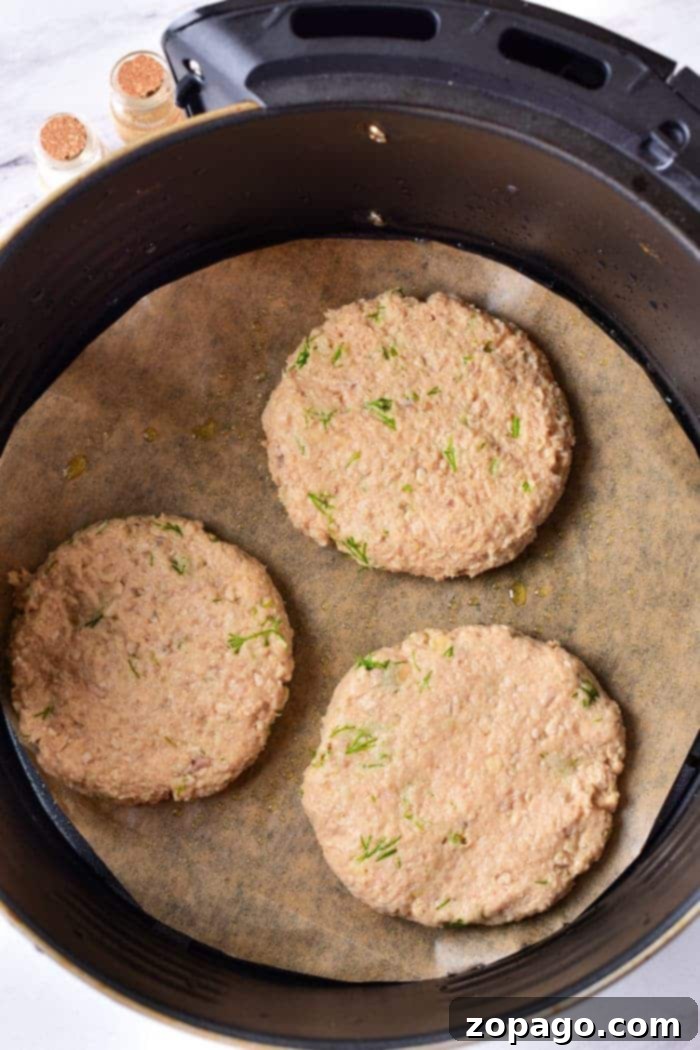 Elevate Your Ground Turkey 3 Three raw turkey burger patties in an air fryer with a parchment paper lining, ready to transform into a delicious meal. Curious about how long to cook ground turkey? It's simple—just adjust the time for juicy goodness and enjoy perfectly cooked patties every time.