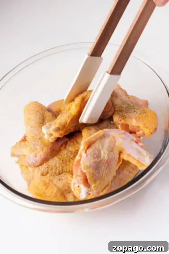 How Long to Bake Crispy Chicken Wings 5 A glass bowl contains several raw chicken wings seasoned with spices.