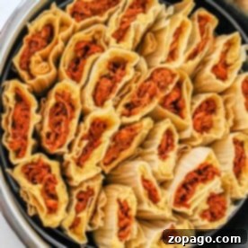 A pot filled with neatly arranged, uncooked red tamales wrapped in corn husks.