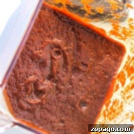Close-up of a blender filled with thick, blended tamale sauce, rich in vibrant red hues.