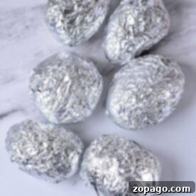Foil-Wrapped Baked Potatoes 4 Six potatoes wrapped in aluminum foil rest on a marble surface, ready to be baked