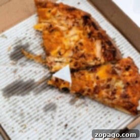 Open pizza box with two slices of baked pizza on a greasy cardboard base, perfect for a quick reheat in the toaster oven.