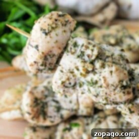 Chicken kabobs in oven, marinated with herbs and spices, stacked on a wooden board.