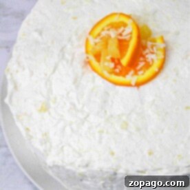 Tropical Paradise Cake 6 White frosted cake topped with vibrant orange slices and a sprinkle of shredded coconut, reminiscent of a luscious Hawaiian Pineapple Cake, presented elegantly on a white plate.
