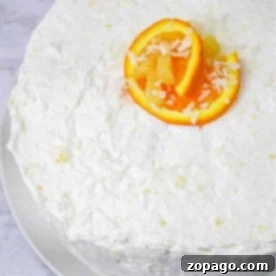 White frosted cake topped with vibrant orange slices and a sprinkle of shredded coconut, reminiscent of a luscious Hawaiian Pineapple Cake, presented elegantly on a white plate.