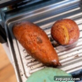 Baked sweet potato and potato on a metal oven tray with an oven mitt nearby, perfect for those who enjoy baking potatoes in a toaster oven.