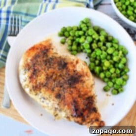 Grilled chicken breast with pepper and herbs, perfectly cooked on the stove, served with peas on a white plate, next to a blue plaid napkin.