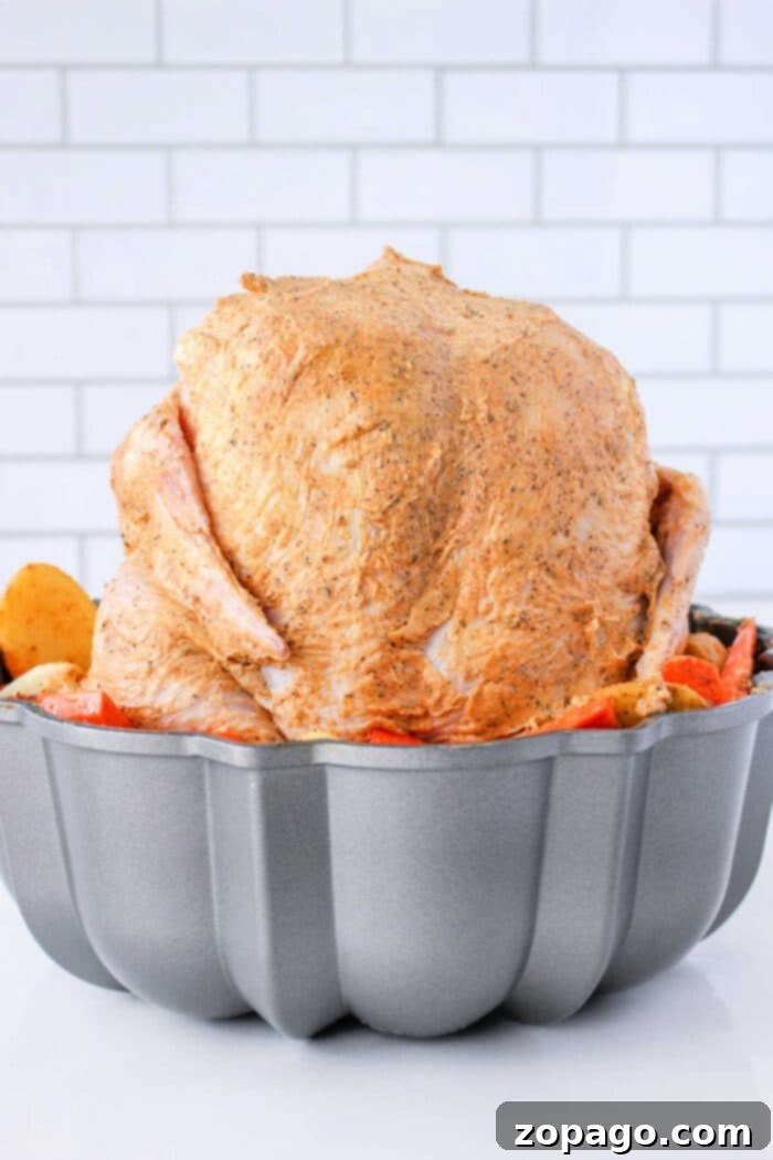 Perfect Chicken Cooking by the Pound 6 A whole roasted chicken standing upright on a bundt pan, surrounded by roasted vegetables