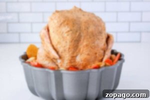 Cooking a Whole Chicken: Timing Per Pound 9 A whole seasoned chicken sits upright in a bundt pan, surrounded by perfectly sliced potatoes and carrots. Wondering how long to cook a whole chicken like this? The backdrop is a simple white tile wall, adding an elegant touch.