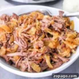Effortless Slow Cooker Pot Roast 7 A bowl of shredded beef with sliced onions sits next to a slow cooker, infused with the rich flavors of red wine, on a gray cloth.