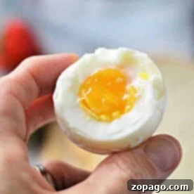 A hand holding a half-peeled soft-boiled egg reveals a perfectly runny yolk, the result of knowing just how long to cook soft boiled eggs on the stove.