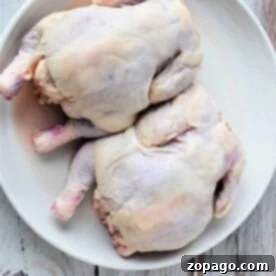 Perfect Cornish Hen Roasting Times 7 Two whole uncooked cornish hens rest on a white plate against a rustic wooden background, inviting the question: how long to cook Cornish hens to achieve that perfect balance of tenderness and flavor?.