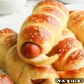 Soft pretzel-wrapped hot dogs stacked on a plate, with ketchup and mustard in bowls in the background—perfect for anyone wondering how long to cook pigs in a blanket for that golden, delicious finish.