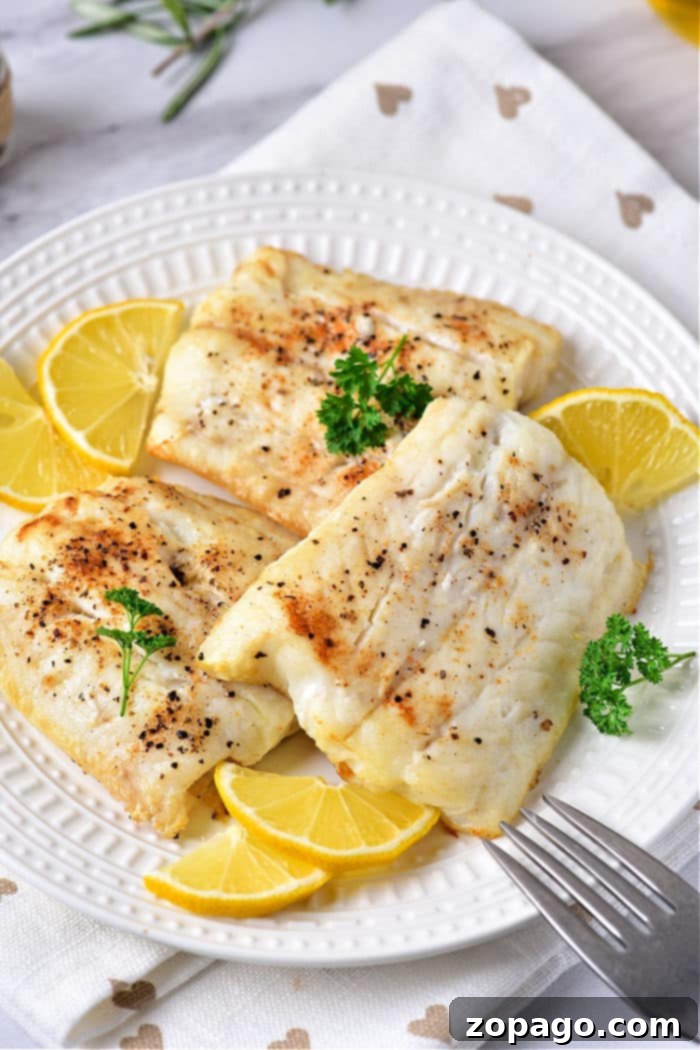 How Long Does Cod Take to Cook 5 baked cod fillets delicately cooked to perfection, paired with lemon slices and parsley on a white plate.