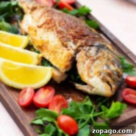 A beautifully cooked whole fish, golden-brown and garnished with fresh herbs and lemon, presented on a wooden board for a delightful meal.