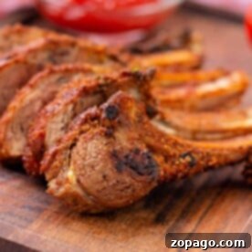 Irresistible Lamb Ribs 7 Grilled, seasoned lamb ribs rest on a wooden board, accompanied by a bowl of red dipping sauce in the background—an inviting glimpse into how to cook lamb ribs to perfection.