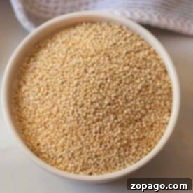 A bowl filled with uncooked quinoa rests on a countertop, accompanied by a textured cloth, all poised to reveal just how long to cook quinoa for that perfect fluffy texture.