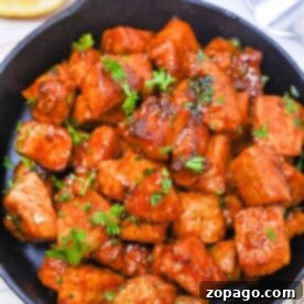 Delicious Pork Bites Made Easy 5 Pork bites, glazed with a savory sauce in a skillet, are garnished with fresh herbs and served alongside lemon slices, with forks at the ready for easy dining.