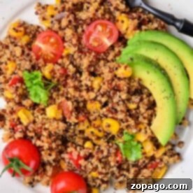 Tri Color Quinoa salad with cherry tomatoes, corn, avocado slices, and a fork elegantly displayed on a white plate.
