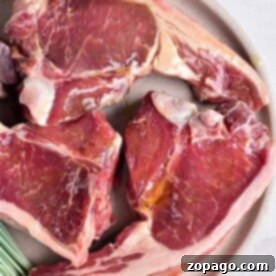 Three raw lamb chops elegantly arranged on a round beige plate, inviting you to ponder how long to cook lamb chops for the perfect tenderness.