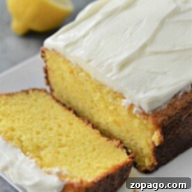 A frosted lemon pound cake with a slice cut, perched invitingly on a white plate, hints at its delightful origin using cake mix. A whole lemon sits artfully in the background, adding a touch of zest to the scene.
