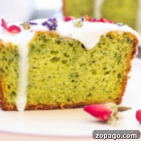 Close-up of a avocado cake slice with white icing and dried flower petals on top, complemented by rosebuds nearby, artfully reminiscent of an avocado cake.