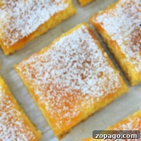 A close-up of lemon bars with cake mix, dusted with powdered sugar on a parchment-lined surface.