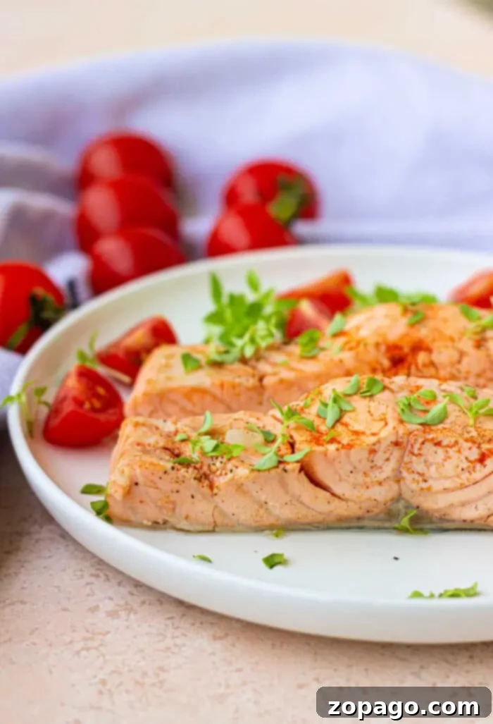 Poached Fish 2 A plate with baked salmon garnished with herbs, accompanied by sliced cherry tomatoes, evokes a delightful blend of flavors. A light-colored cloth and whole cherry tomatoes sit in the background, offering a fresh contrast reminiscent of boiled fish simplicity.