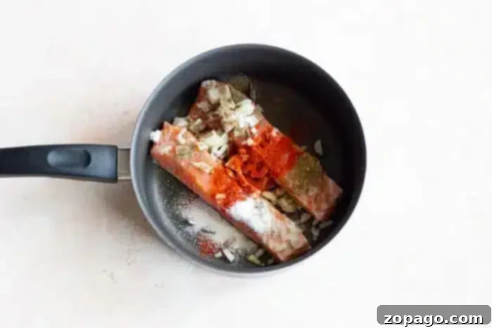 Poached Fish 4 Two pieces of salmon sizzle in a pan, topped with salt, pepper, chopped onion, and red spices, capturing the essence of perfectly seasoned boiled fish.