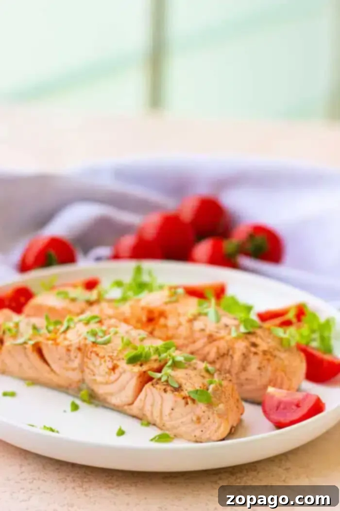 Poached Fish 6 A plate with two fillets of salmon, reminiscent of delicately boiled fish, garnished with fresh herbs. Cherry tomatoes and sprigs of parsley are artfully arranged around the salmon. A light-colored cloth is in the background, along with whole tomatoes.