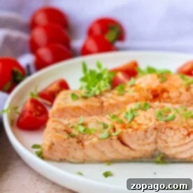 Salmon garnished with fresh herbs graces a white plate, evoking the subtle aroma of boiled fish, while cherry tomatoes add a pop of color in the background.