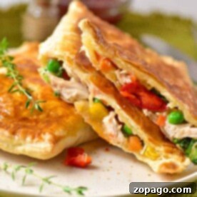 Golden savory hand pies filled with chicken, peas, corn, and diced red peppers are served on a white plate garnished with fresh herbs.