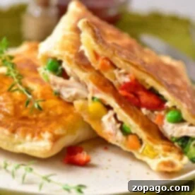 Golden savory hand pies filled with chicken, peas, corn, and diced red peppers are served on a white plate garnished with fresh herbs.