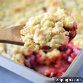 Easy Cake Mix Cherry Cobbler 6 A wooden spoon lifts a scoop of cherry cobbler with cake mix above a baking dish brimming with more crumble, teasing the senses with its warm, inviting aroma.