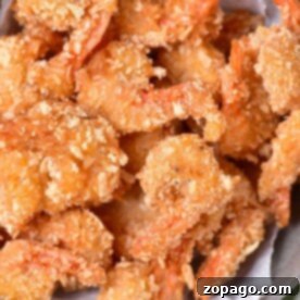 A bowl of golden, crunchy coconut shrimp sits on parchment paper, perfectly fried to a crisp.