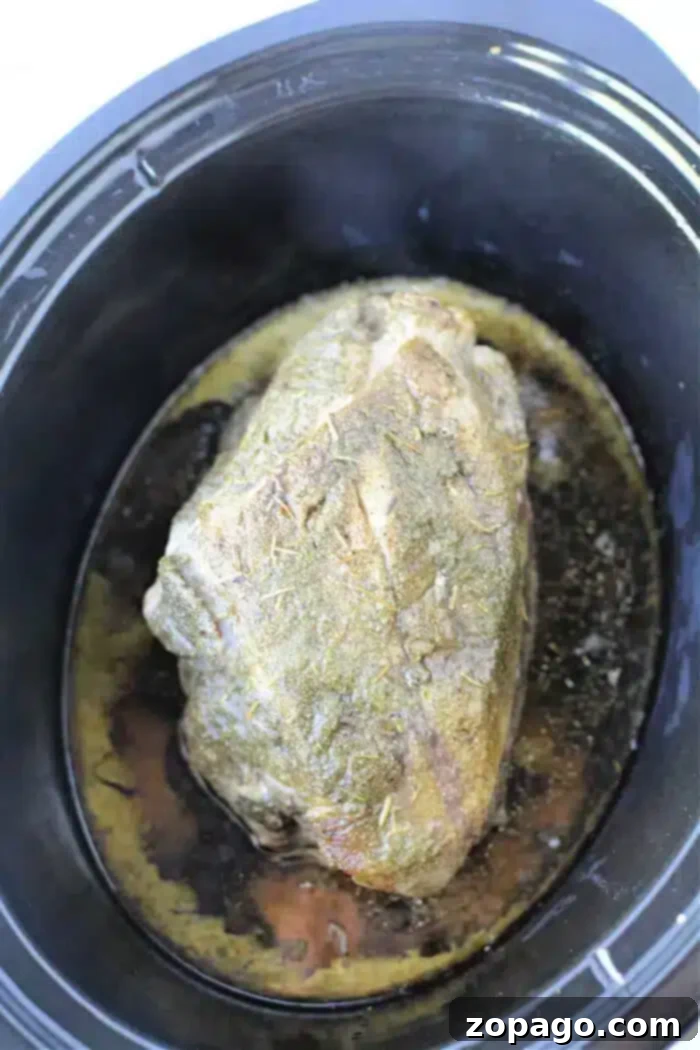 Easy 3-Ingredient Slow Cooker Pork Roast 5 A black slow cooker contains a tender, 3 Ingredient Pork Roast Slow Cooker bone-in pork shoulder roast. The roast is seasoned with herbs and sits in its juices at the bottom of the cooker.