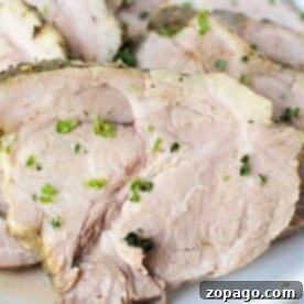 Savor tender slices of cooked pork enhanced with herbs, perfectly prepared using a 3 ingredient recipe in a slow cooker, elegantly presented on a white plate.
