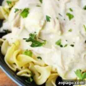 Instant Pot creamy chicken pasta topped with a luscious white sauce and garnished with chopped parsley in a dark bowl.