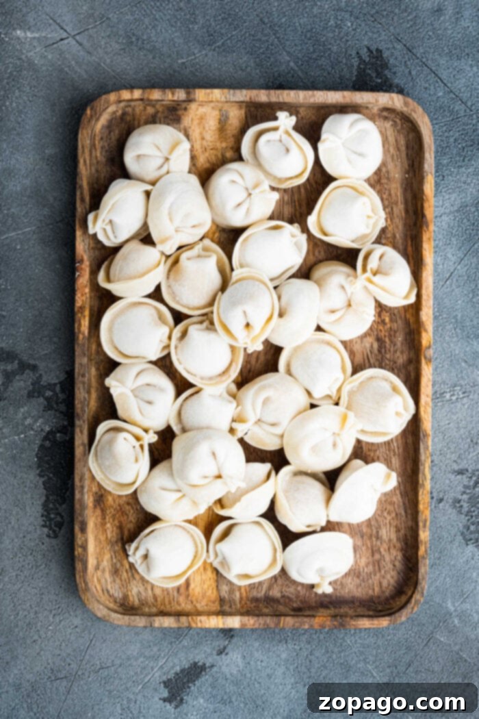 Easy Frozen Tortellini Meals 3 A rustic wooden tray neatly arranged with uncooked frozen tortellini against a textured gray background, inspiring delicious Crockpot recipes with tortellini.