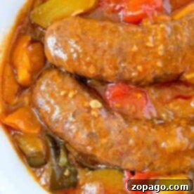 Sausages in a tomato sauce with red and green bell peppers, all simmered to perfection in a crockpot, served in a white bowl.